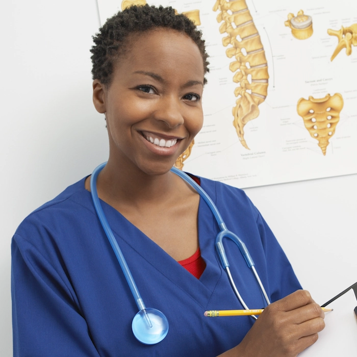 Smiling female doctor wearing blue scrubs and a stethoscope around her neck holding a pencil and clipboard